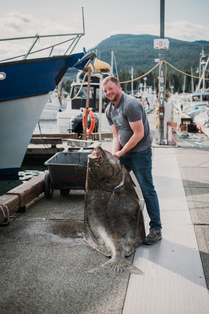 man lifting monster halibut on dock in juneau alaska