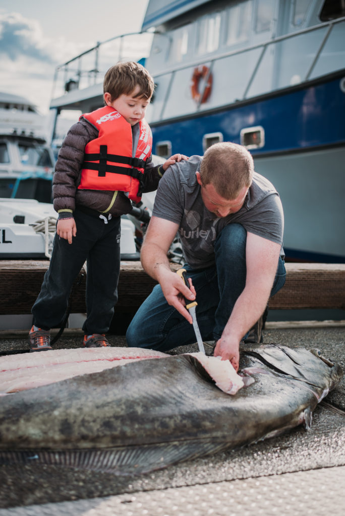 boy on dock watching father fillet monster halibut