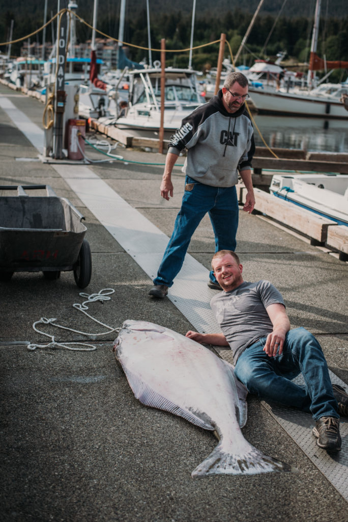 6 foot long halibut with man laying next to it