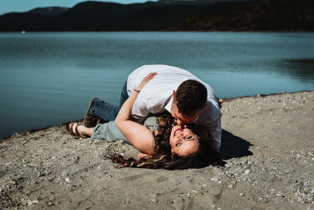 couple rolling around in the sand man kissing woman on the cheek while she smiles