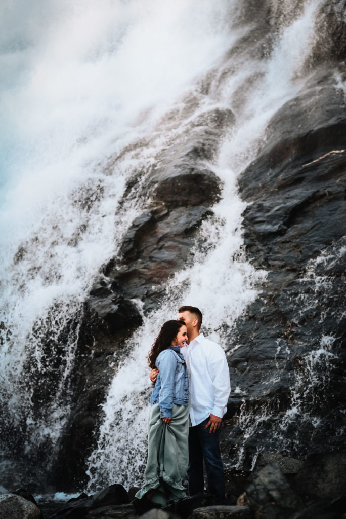 couple standing closely in front of waterfall