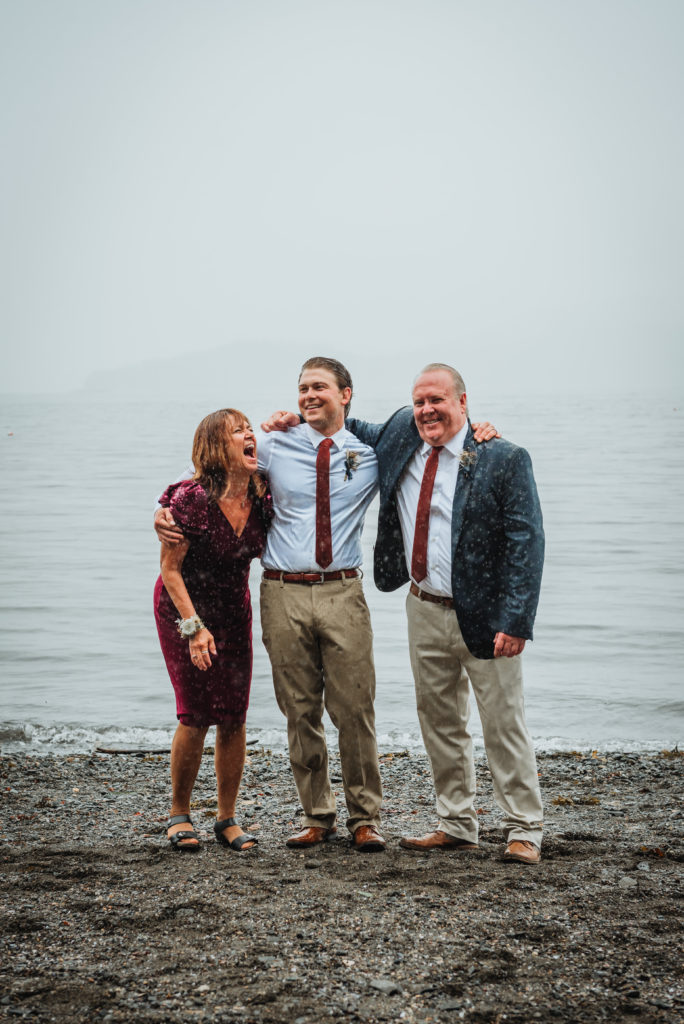 groom with his parents mom and dad laughing in a foggy background.