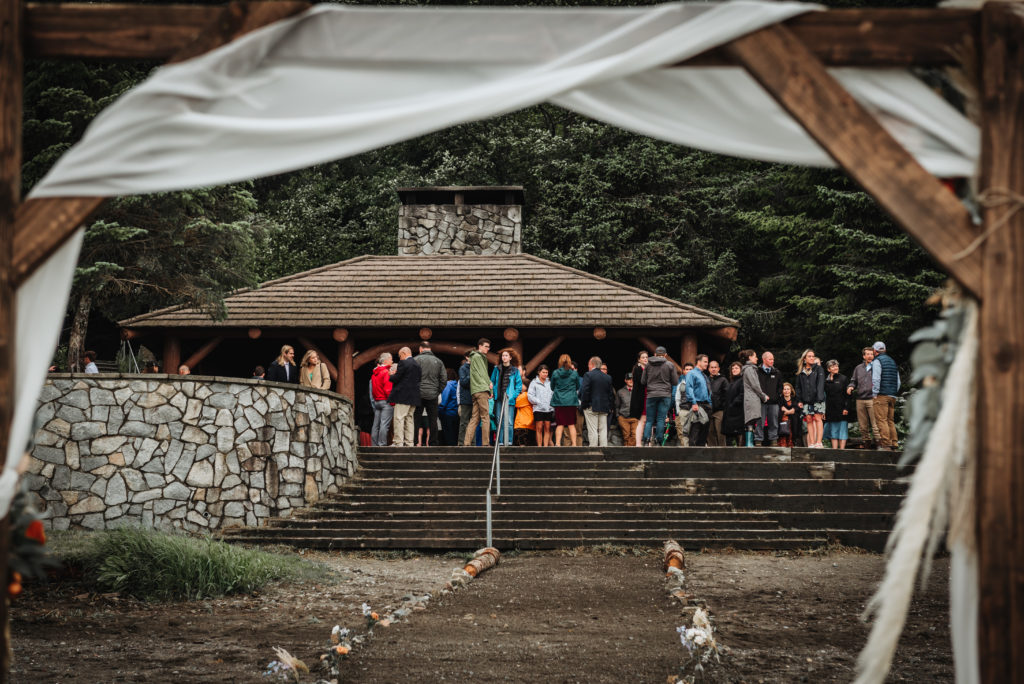 wedding guests gathering near a cabin framed by arch