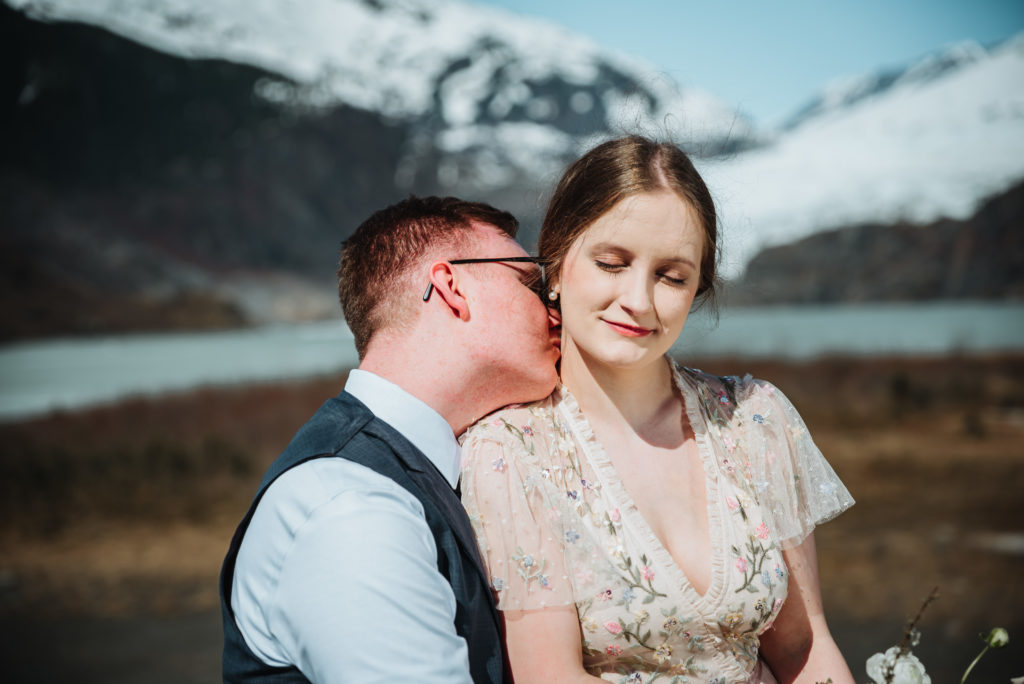 groom kissing bride smiling in front of mendenhall glacier 