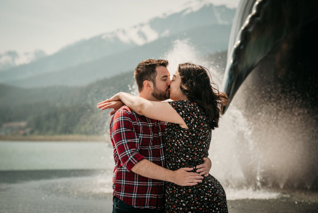 engaged couple kissing with fountains at the whale statue in juneau alaska