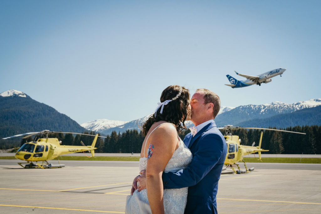 bride and groom kiss as alaska airlines plan flies overhead