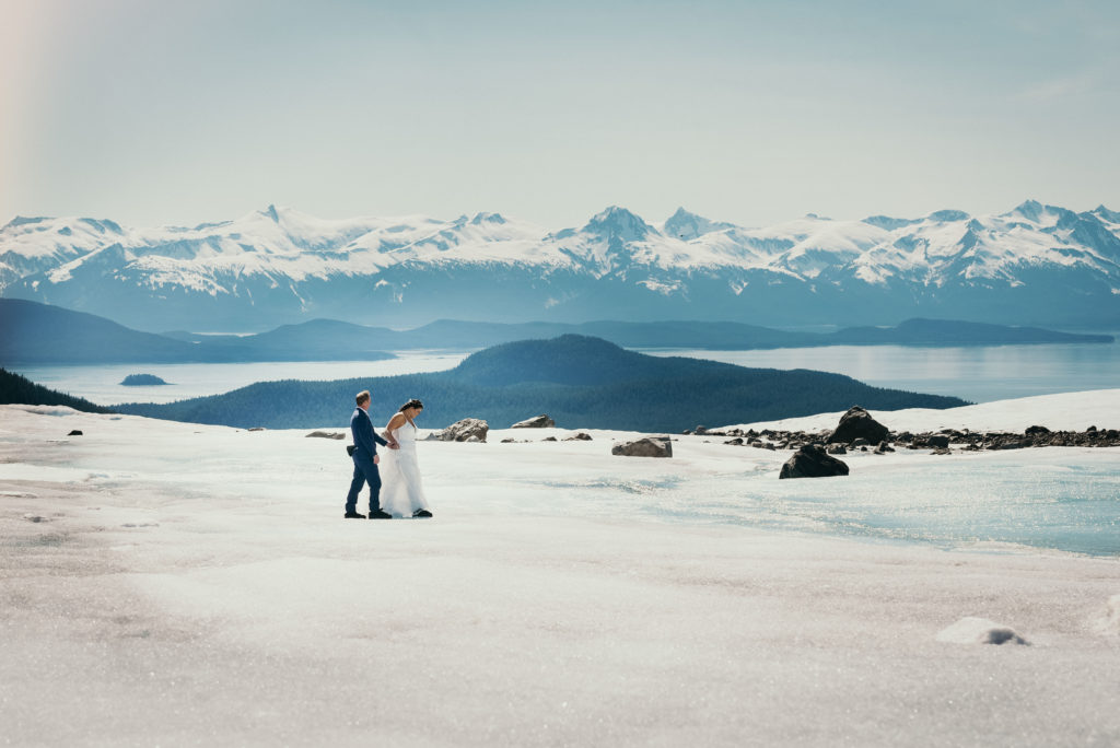bride and groom walking on juneau glacier with epic background