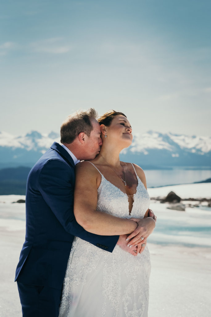 groom kissing brides neck on glacier