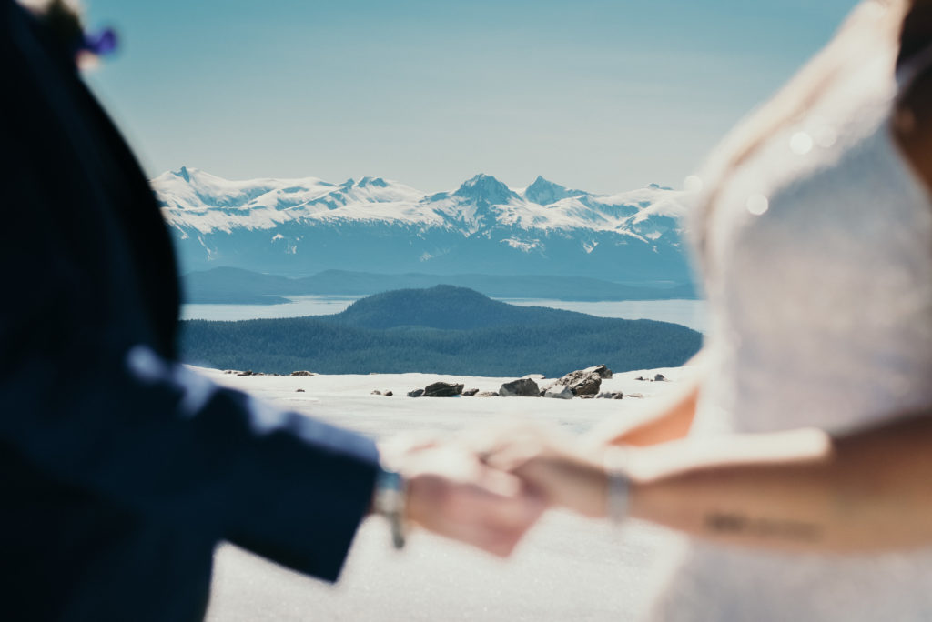 bride and groom holding hands duing alaska glacier wedding with background in focus