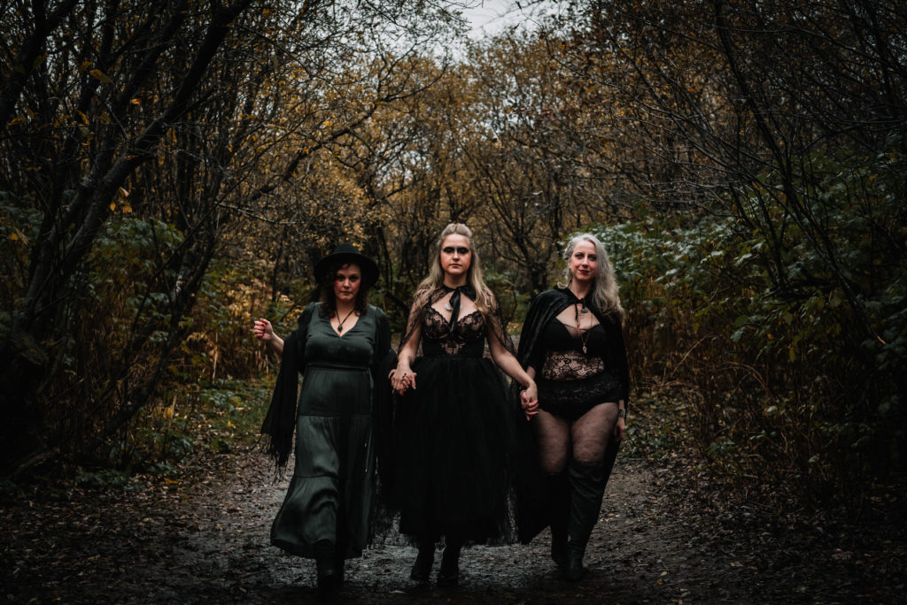 three witches in black walking along trail during styled shoot