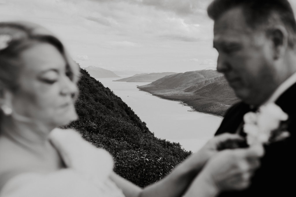 Bride securing grooms Boutonnière during alaska mountaintop elopement with gastineau channel in background