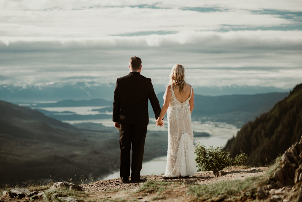 bride and groom in front of epic mountaintop view of juneau alaska