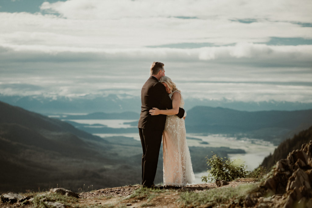 bride and groom hug in front of epic view of channel in juneau alaska