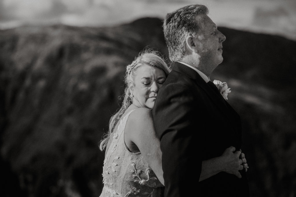 black and white photo of bride hugging groom from behind on mountaintop