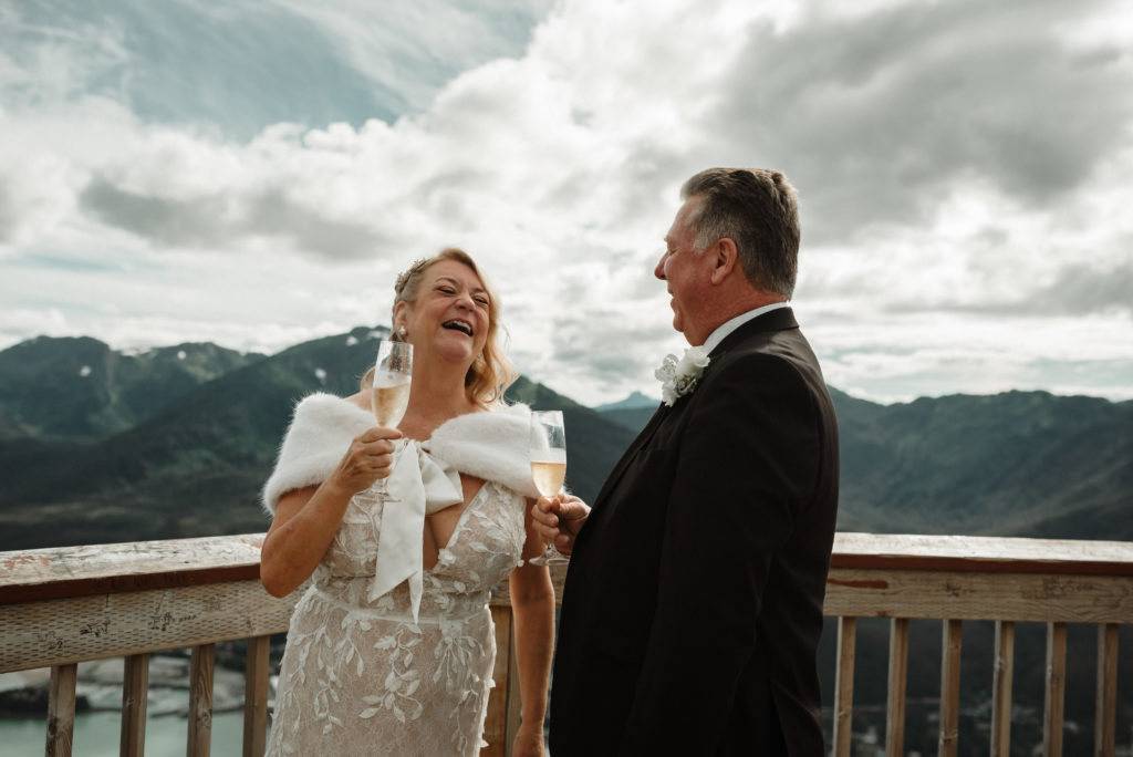 bride and groom drinking champagne and laughing after eloping on a mountaintop in juneau alaska