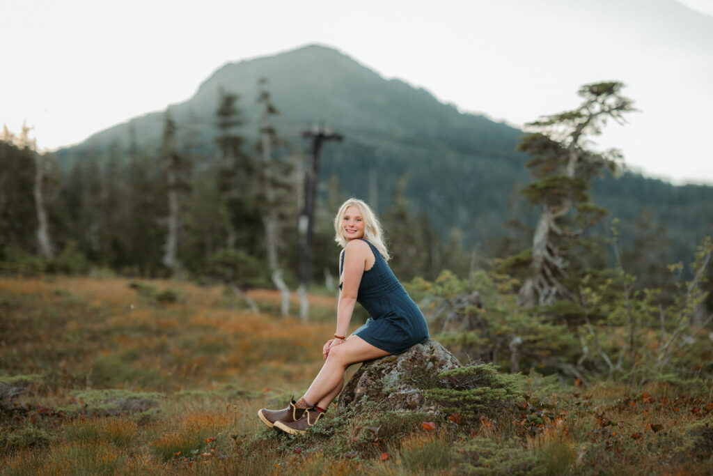 senior girl sitting on a rock in a meadow at eaglecrest ski resort in the summer