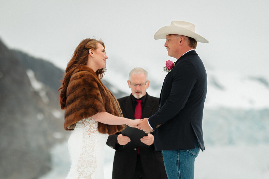 couple exchanging vows on mendenhall glacier during alaska elopement wearing cowboy hat and cowboy boots