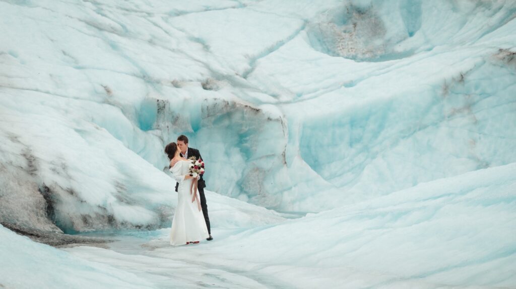 bride and groom in front of blue ice wall on spencer glacier alaska